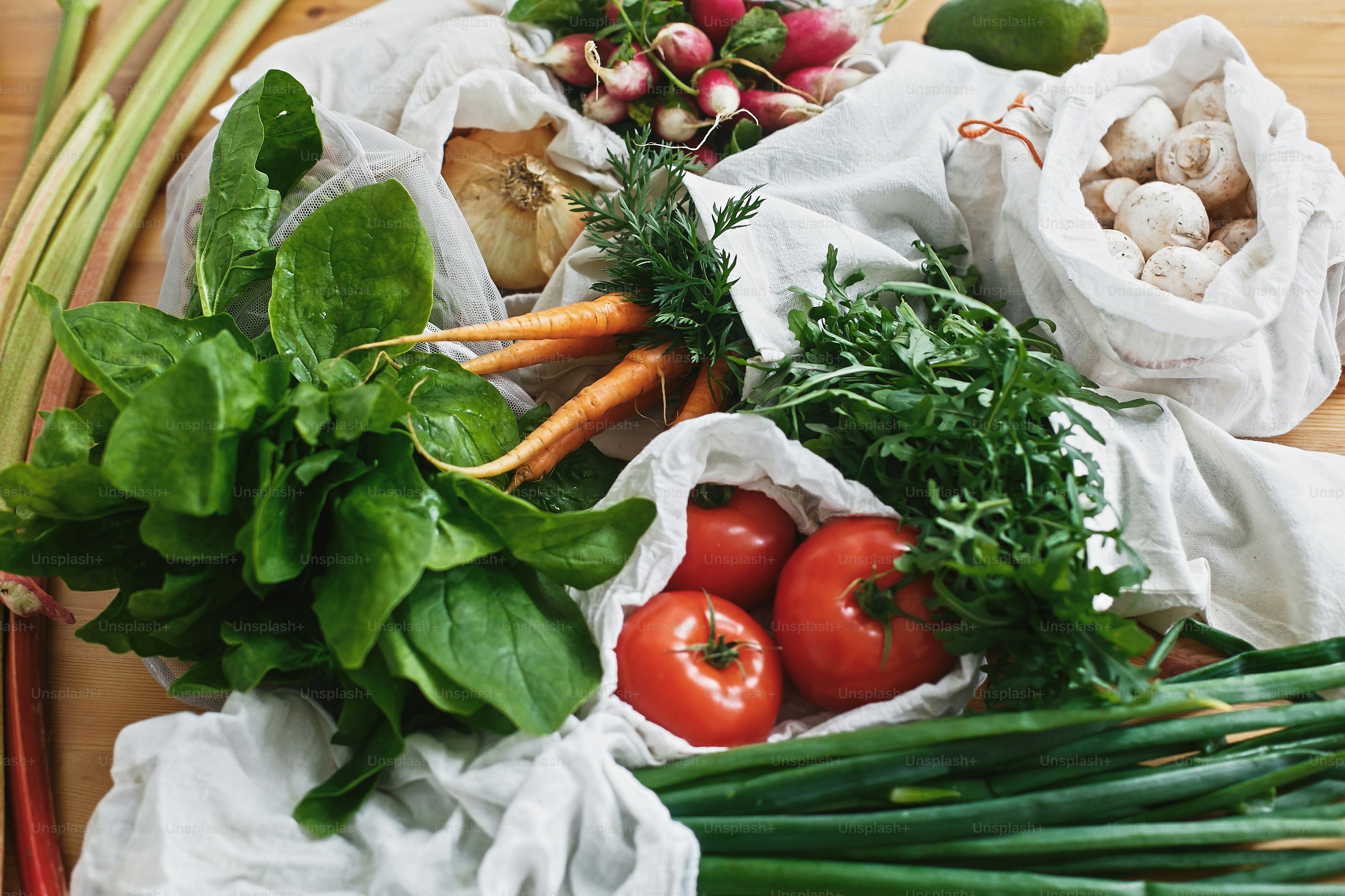 Tas ramah lingkungan yang dapat digunakan kembali dengan sayuran segar, wortel, tomat, bayam, arugula, jamur, rhubarb, bawang di atas meja kayu. melarang plastik. Konsep belanja bahan makanan tanpa limbah