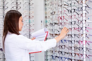 クリップボードにデータを書き込む魅力的な女性眼科医が、眼鏡店で働いています。ヘルスケアと医療のコンセプト