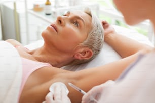 Underarm injection. Nice short haired woman receiving an injection while visiting a beauty clinic for treatment