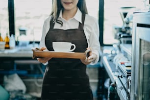 Donna barista che serve tazza di caffè al bar, barista asiatica che tiene il caffè servito con faccia sorridente.