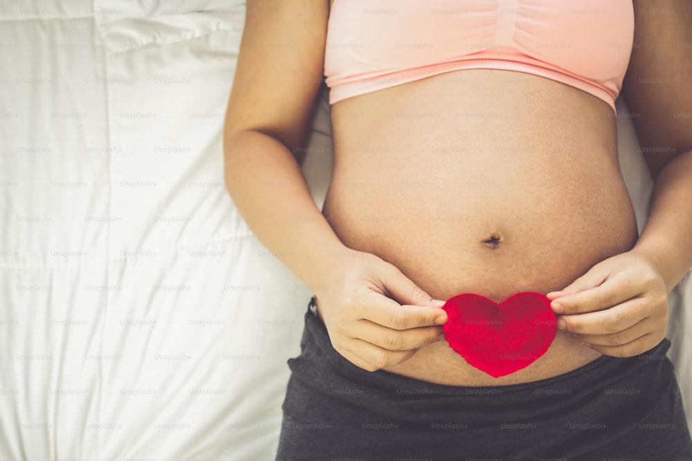 Pregnant woman feeling happy at home while taking care of her child. The young expecting mother holding baby in pregnant belly. Maternity prenatal care and woman pregnancy concept.