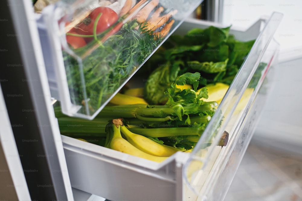 Zanahorias, tomates, champiñones, plátanos, ensalada, espinacas, apio, manzanas sin plástico en el refrigerador. Compras de comestibles sin desperdicio. Verduras frescas en el cajón abierto del refrigerador. Dieta vegetariana