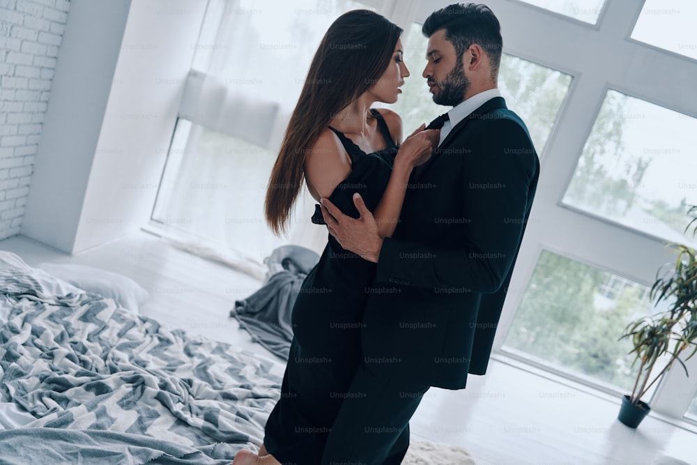 Hübscher junger Mann, der seine Freundin küsst und auszieht, während er im Schlafzimmer steht