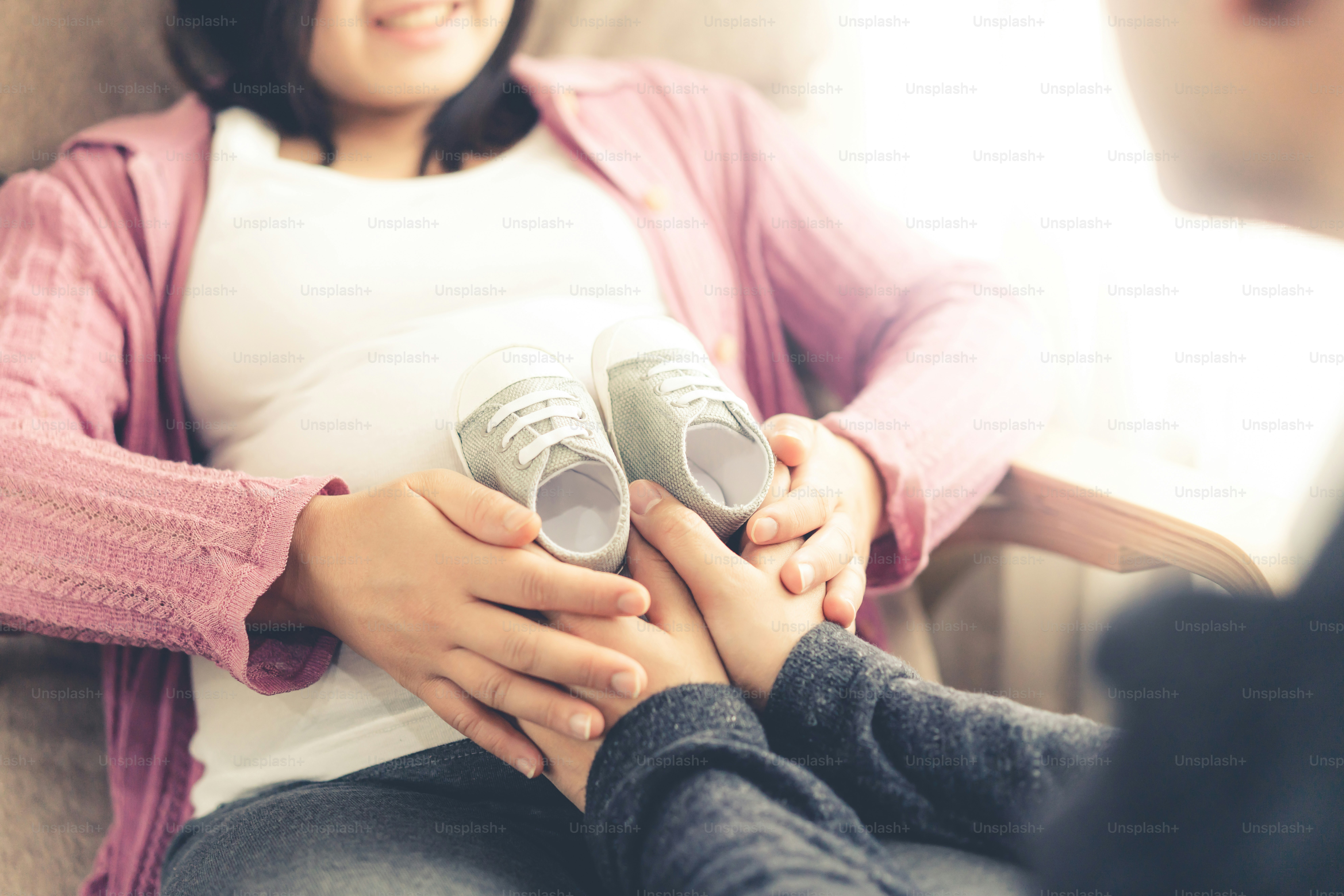 Pregnant couple of husband and wife feels love and relax at home. Young expecting woman holds baby in pregnant belly. Father take care of pregnant mother. Concept of maternity and pregnancy care.