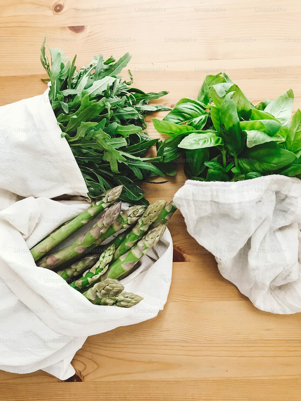 Zero waste grocery shopping concept. Reusable eco friendly bags with fresh asparagus, arugula,spinach,basil on wooden table, top view. Ban plastic. Choose plastic free.