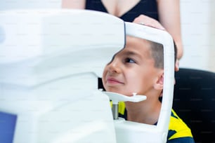 Oculiste féminine utilisant une machine pour vérifier la vue en clinique. Petit garçon regardant l’équipement et le médecin testant la pupille oculaire dans un magasin d’optique. Concept de soins oculaires et de santé