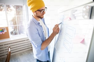 Young creative man writing down ideas on wall full of sticky notes. Brainstorming concept