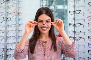 Gesundheits-, Seh- und Sehkonzept - glückliche Frau wählt Brille im Optikgeschäft.
