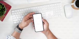 Man's hand holding white screen mobile phone on desk in office