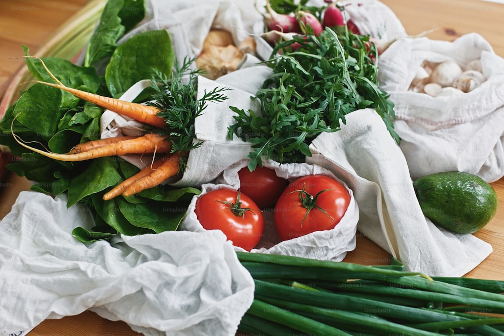 Concept d’épicerie zéro déchet. Sacs écologiques réutilisables avec des légumes frais, des carottes, des tomates, de la roquette, des champignons du marché sur une table en bois. Bannissez le plastique. Mode de vie durable.