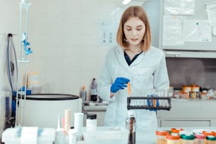 Medical lab. Intelligent young woman taking test tubes for examination while working in the medical lab