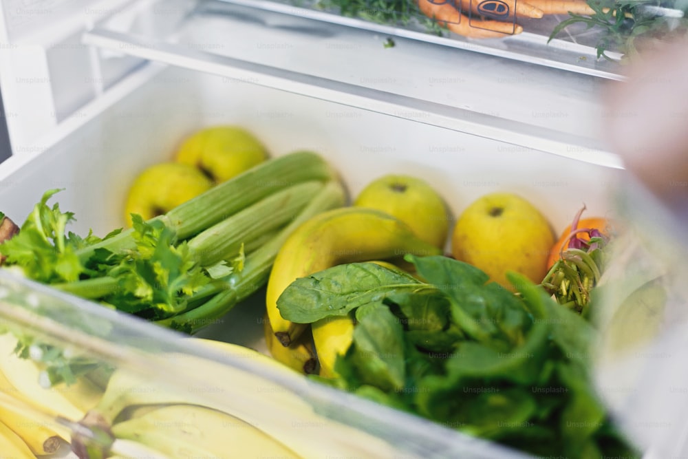 Plastikfreie Bananen, Salat, Spinat, Sellerie, Äpfel, Orange im Kühlschrank. Zero Waste Lebensmitteleinkauf. Frisches Gemüse in geöffneter Schublade im Kühlschrank. Vegetarische Ernährung. Lieferung von Lebensmitteln