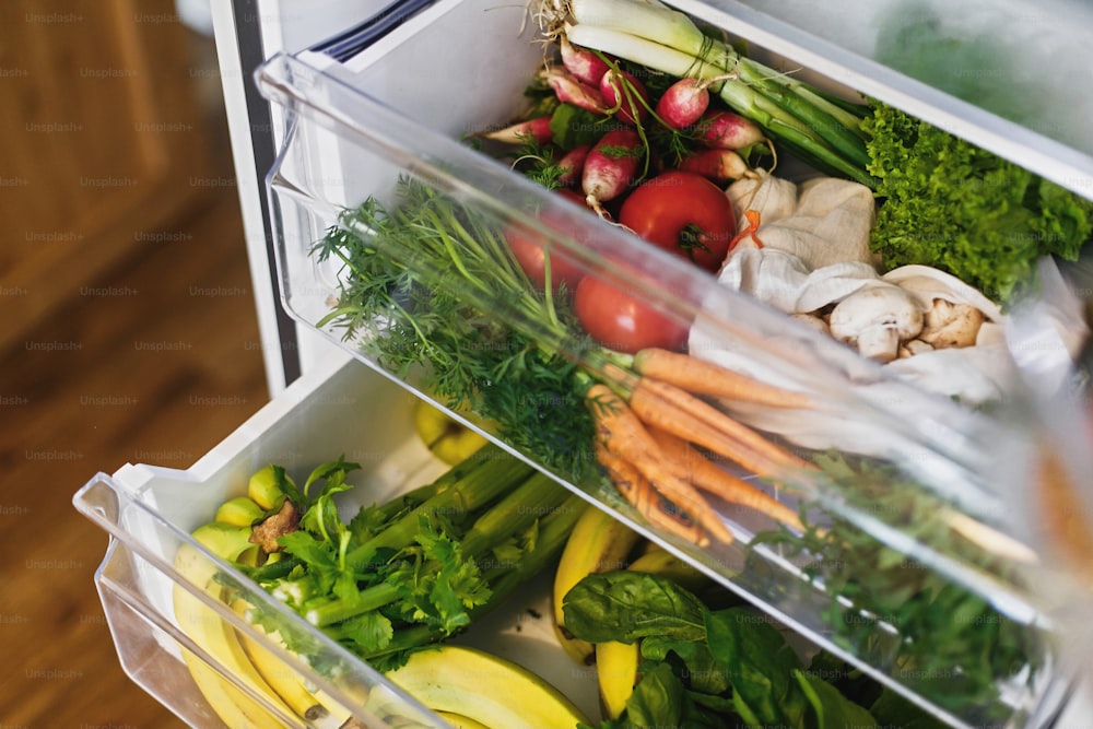 Spesa a spreco zero in frigorifero. Verdure fresche in cassetto aperto in frigorifero. Carote, pomodori, funghi, banane, insalata, sedano, mele, shopping a rifiuti zero. Consegna di generi alimentari