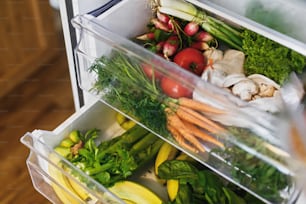 Desperdício zero de mercearia na geladeira. Legumes frescos na gaveta aberta na geladeira. Cenouras plásticas livres, tomates, cogumelos, bananas, salada, aipo, maçãs, compras de lixo zero. Entrega de supermercado