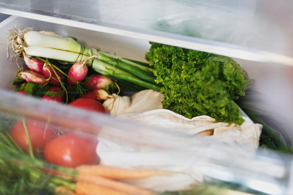 Verduras frescas en el cajón abierto del refrigerador. Zanahorias, tomates, champiñones, cebollas, rábanos, ensaladas, rúculas del mercado en la nevera sin plástico. Concepto de compra de comestibles de desperdicio cero.