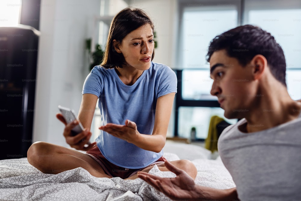 Disappointed woman arguing with her boyfriend about text message on mobile phone.