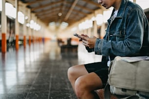 Traveler using mobile phone in train station with backpacker concept.