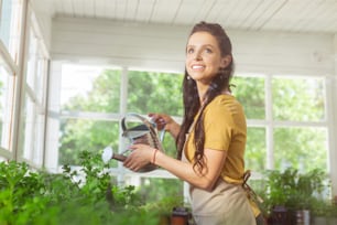 Working day. Smiling beautiful florist watering all of the plants in her flower shop.