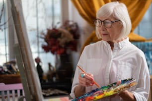 Beautiful woman. Beautiful retired woman wearing glasses holding color palette and brush