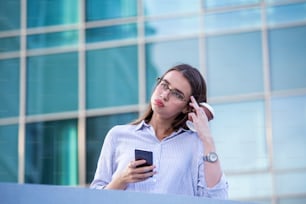Geschäftsfrau erhält schlechte Nachrichten auf dem Smartphone und trinkt Kaffee aus Einweg-Pappbecher auf der Straße mit Bürogebäuden im Hintergrund.
