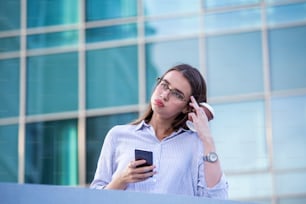 Business woman recieving bad news on smartphone and drinking coffee from disposable paper cup in the street with office buildings in the background.