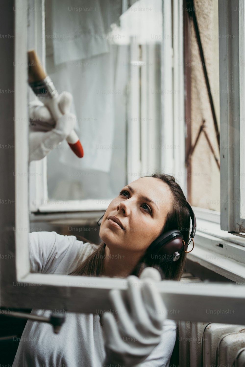 Beautiful and diligent middle age handy woman renovating her old home or apartment. She is holding professional paintbrush and painting windows. Do it yourself housework concept.