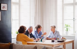Grupo de personas mayores sentadas en la mesa en el club del centro comunitario, jugando juegos de mesa.