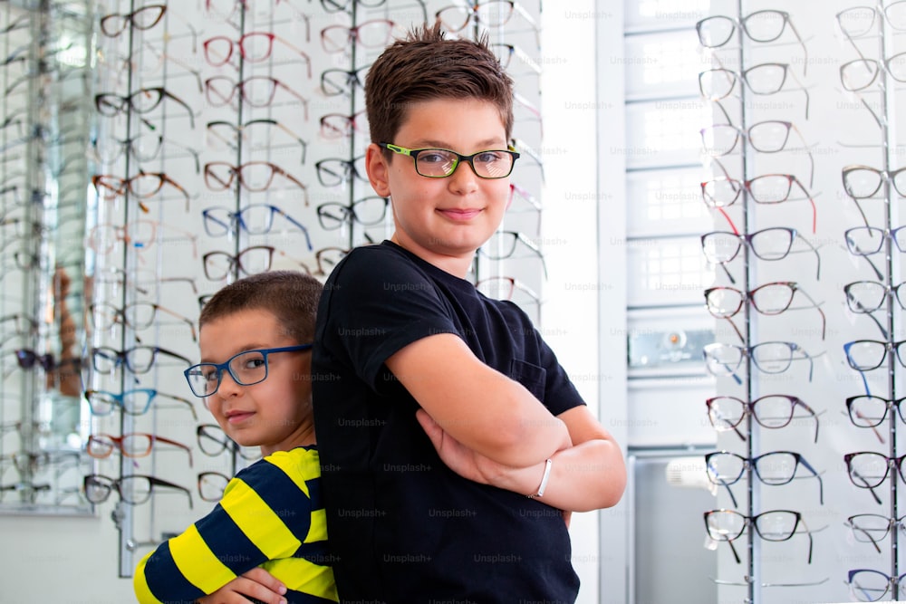 Gesundheits-, Seh- und Sehkonzept - zwei Jungen, die sich im Optikgeschäft für eine Brille entscheiden.