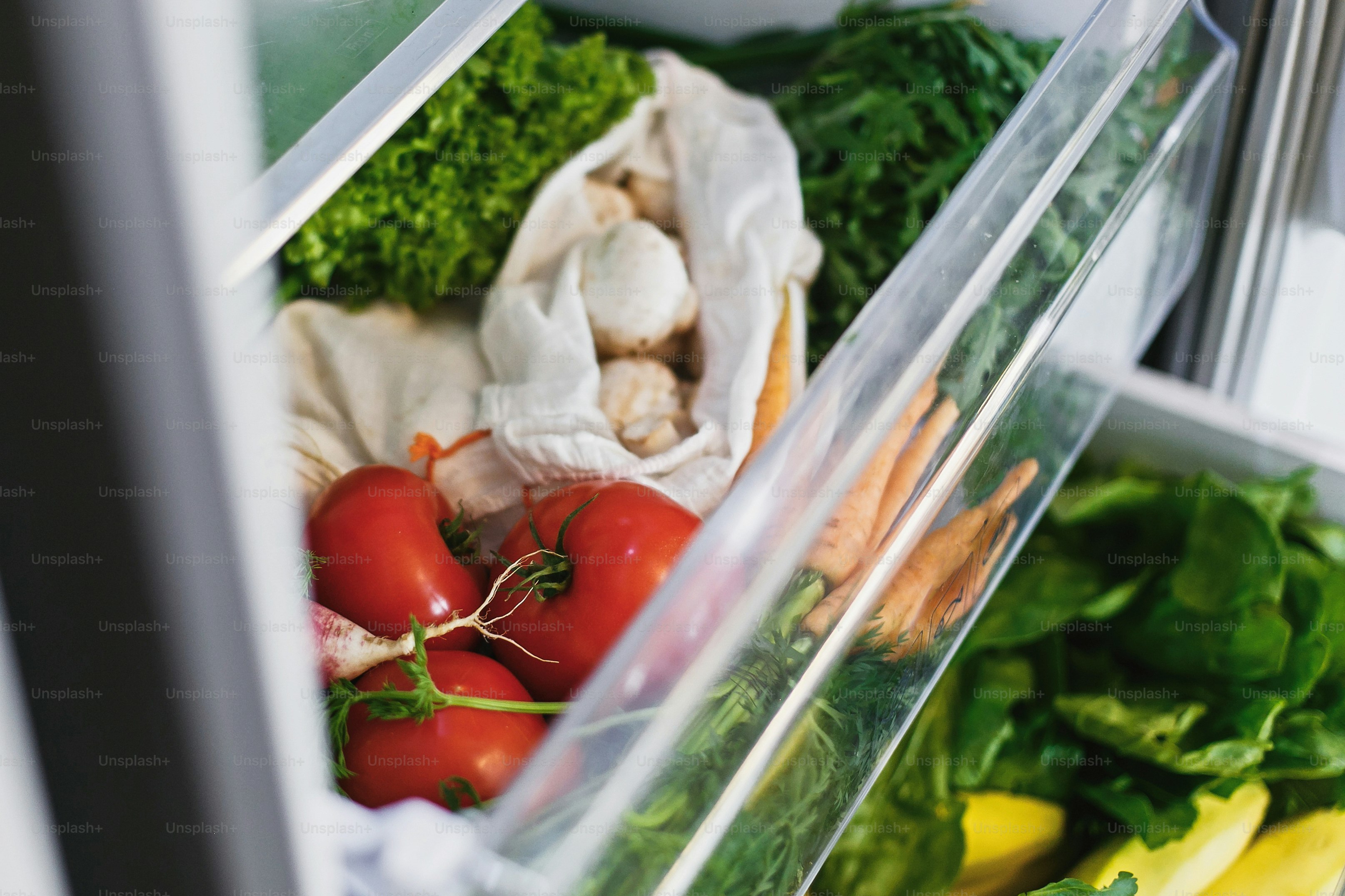 Fresh vegetables including tomatoes, carrots, and leafy greens inside a refrigerator drawer