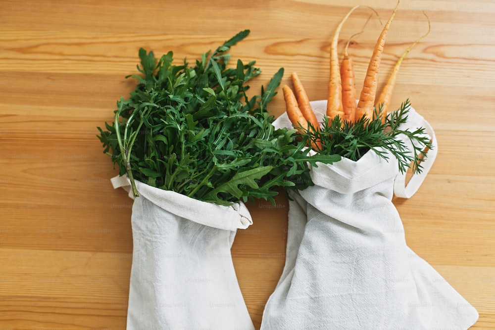 Zero waste grocery shopping concept. Reusable eco friendly bags with fresh vegetables carrots, arugula, on wooden table, flat lay. ban plastic. Sustainable lifestyle.reuse, reduce, recycle