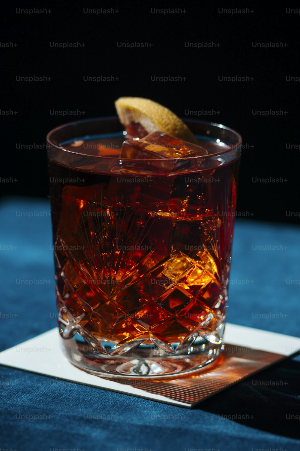 Cocktail Negroni IBA, avec du gin, de l’amer, du vermut et de la tranche d’orance. Fond coloré et sombre.