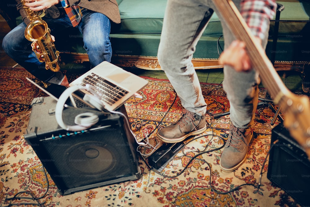 Músicos tendo ensaio em home studio. No chão amplificadores, laptop e fones de ouvido.
