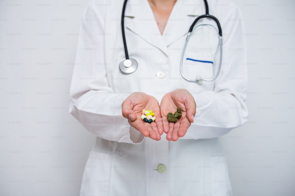 Médico de la mano sosteniendo cogollos de cannabis medicinal y pastillas.