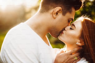 Close up portrait of a amazing caucasian female with freckles and red hair kissing with her boyfriend outside against sunset while traveling.