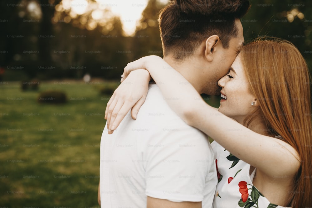 Side view portrait of a lovely young woman with red hair and freckles embracing neck of her boyfriend smiling outside while dating in their vacation time.