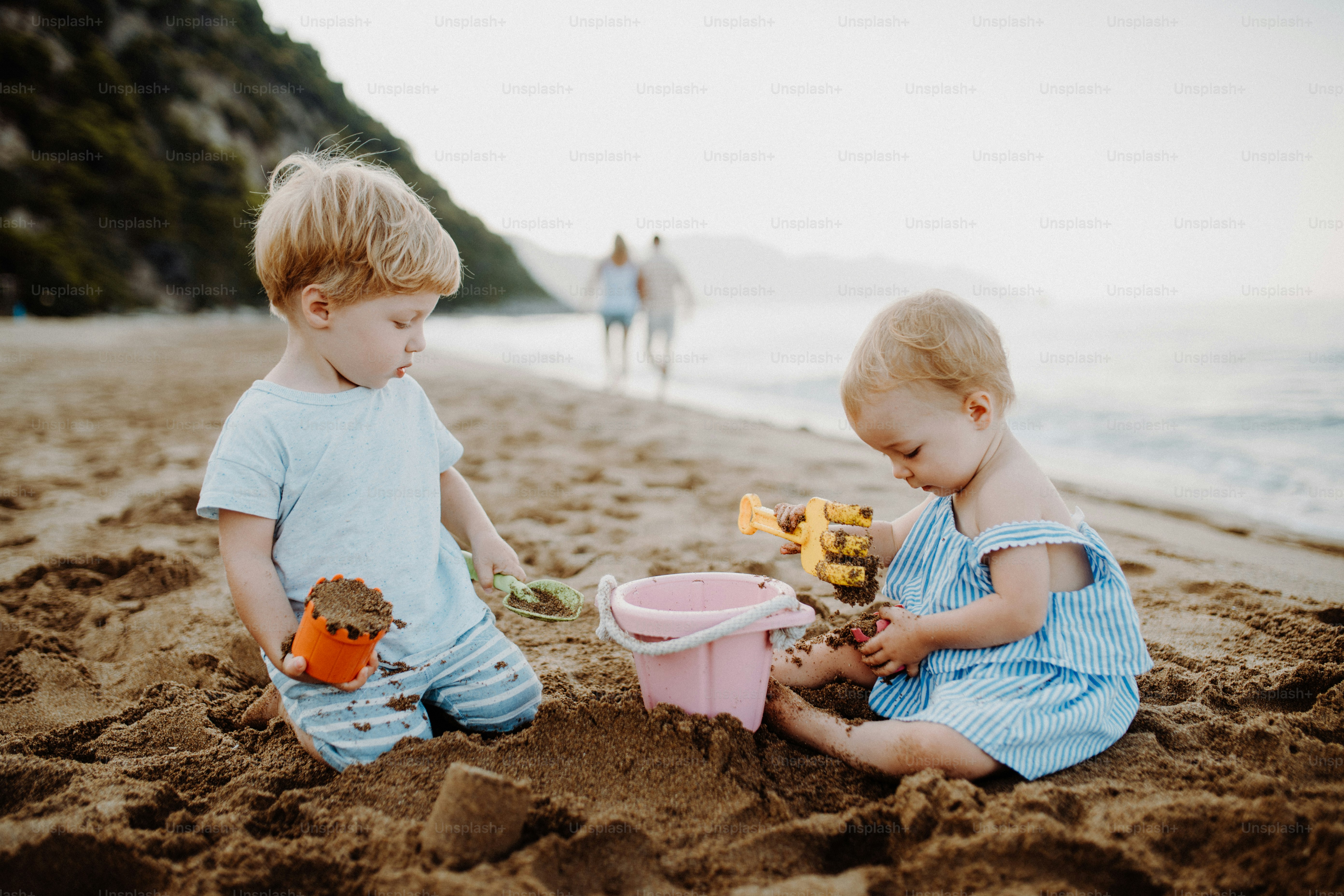Zwei Kleinkinder spielen am Sandstrand im Sommerurlaub mit der Familie.
