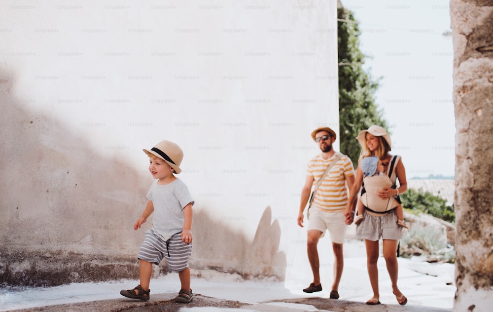 A family with two toddler children walking in town on summer holiday. A father and mother with son and daughter in baby carrier on a street.