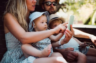 Una giovane famiglia con due bambini piccoli in taxi in auto in vacanza estiva, utilizzando lo smartphone.