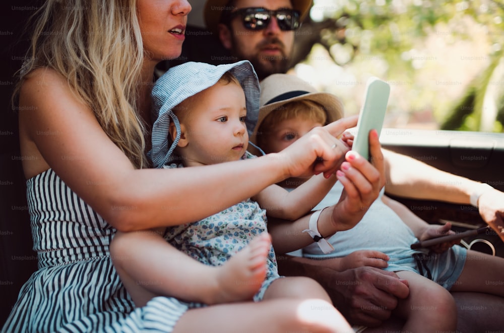 A young family with two toddler children in taxi car on summer holiday, using smartphone.
