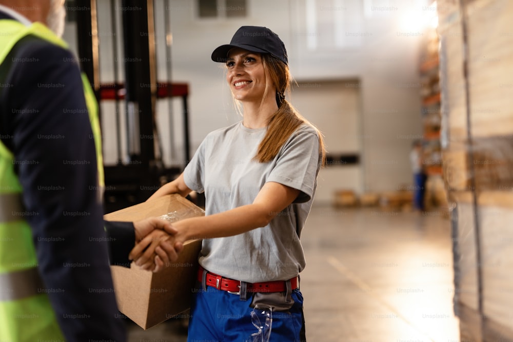 Happy female worker greeting company manager and shaking hands with him in industrial warehouse.