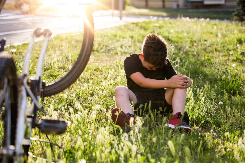 Niño en el suelo de la calle con una lesión en la rodilla gritando después de caerse de su bicicleta