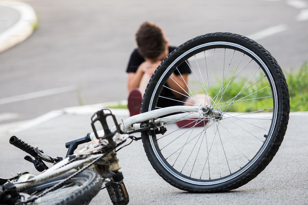 Menino no chão da rua com uma lesão no joelho gritando depois de cair em sua bicicleta
