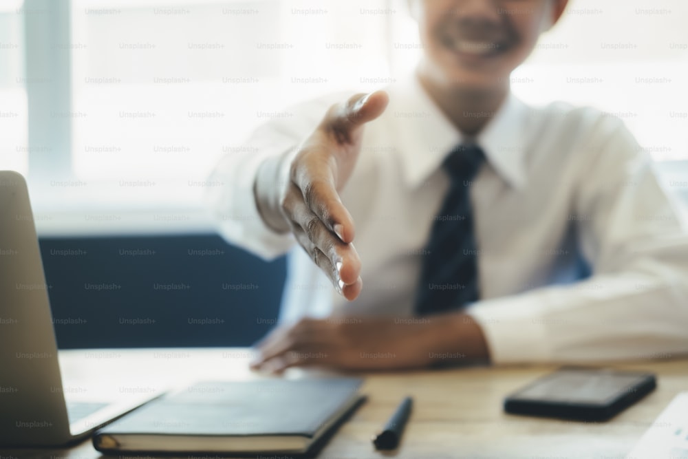 Smiling young Asian businessman executive extending his arm in a handshake to making a success deal with customer or partner.