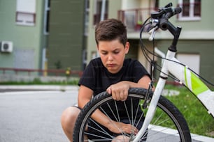 Trauriger Junge, der auf seinen platten Fahrradreifen schaut, Kind, das auf das Fahrrad mit dem kaputten Rad starrt