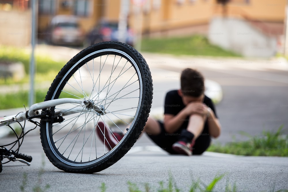 Boy in the street ground with a knee injury screaming after falling off to his bicycle