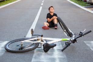 Kid hurts his leg after falling off his bicycle. Child is learning to ride a bike. Boy in the street ground with a knee injury screaming after falling off to his bicycle.