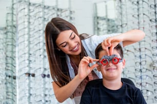 Oftalmologista atraente examinando youg menino com quadro de ensaio optometrista. Paciente criança para verificar a visão na clínica oftalmológica.