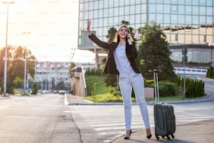 Smiling young woman tries to stop taxi, calling a taxi.