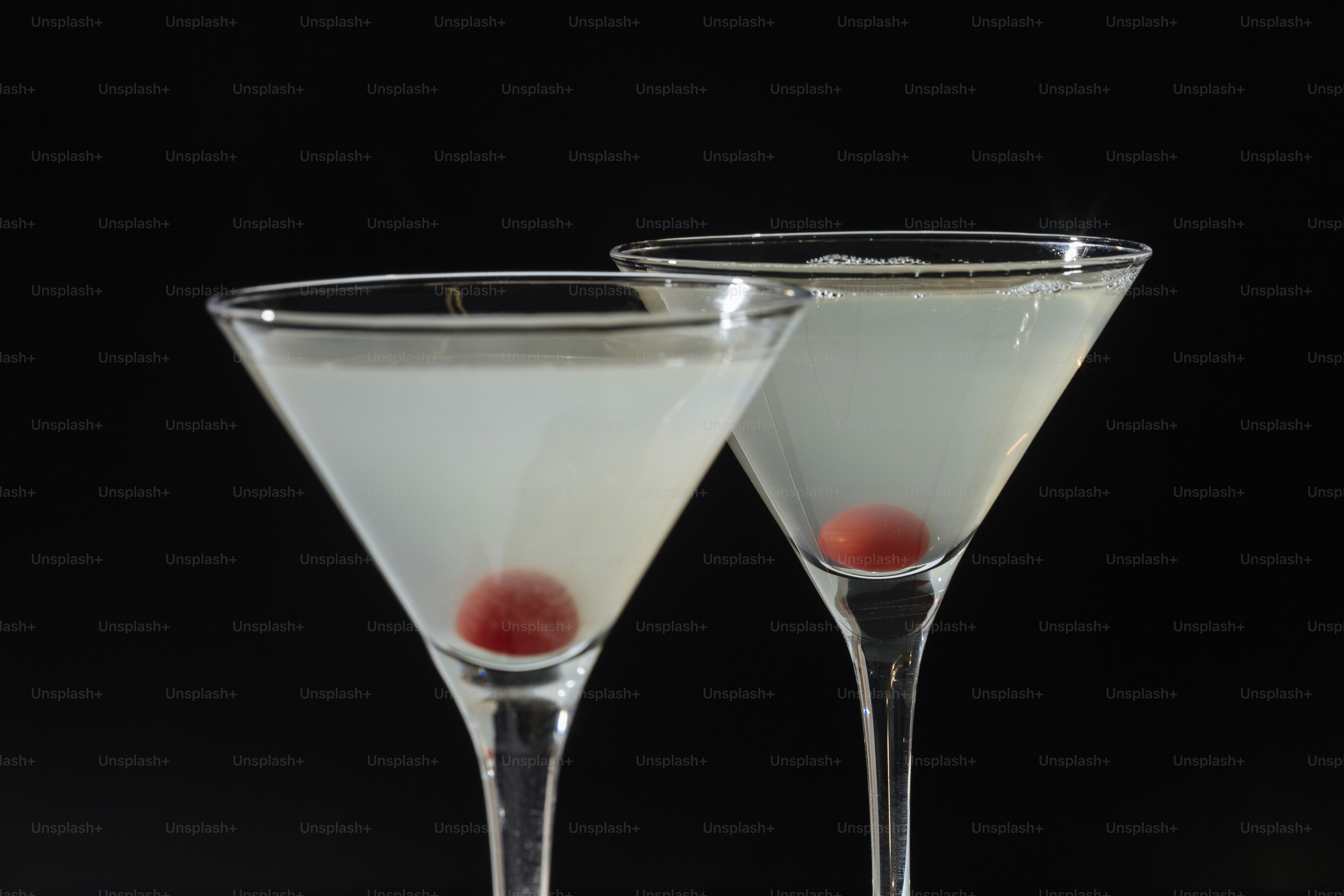 Zwei Martini-Gläser gefüllt mit blasser Flüssigkeit und jeweils eine rote Kirsche