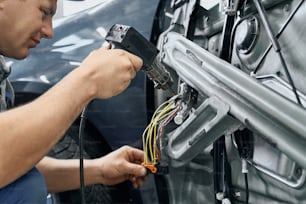 Side view of car electric repairman holding and using the soldering iron to blend the wires for repairing signaling in disassembled door of auto. Servicing of electronic devices concept